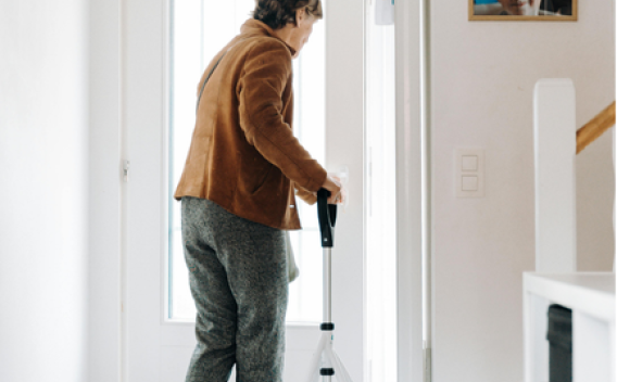 Older adult woman exiting her home with a cane.